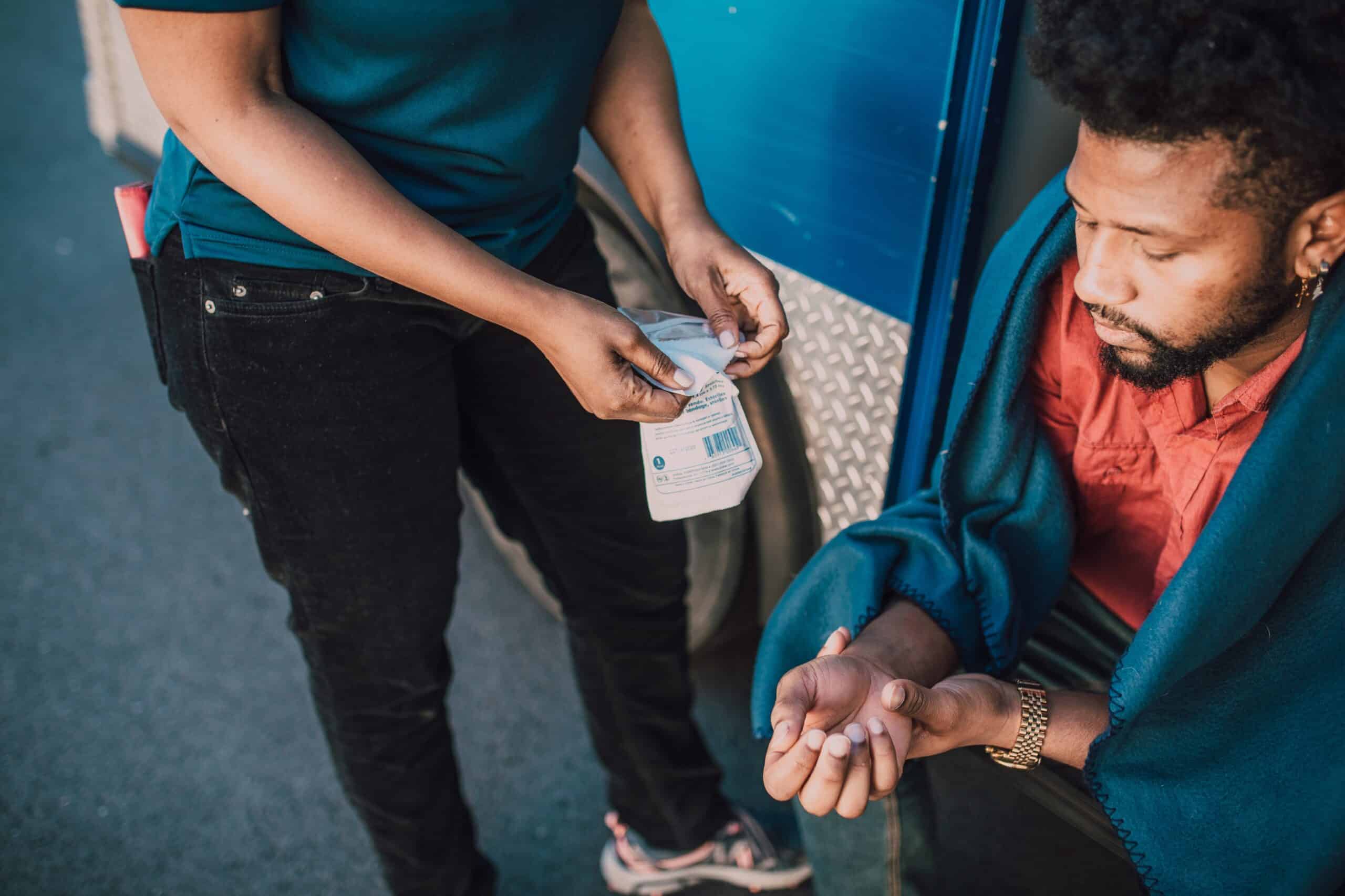 Injured man receiving first aid for an arm injury beside a vehicle, illustrating a personal injury accident and medical care after an incident